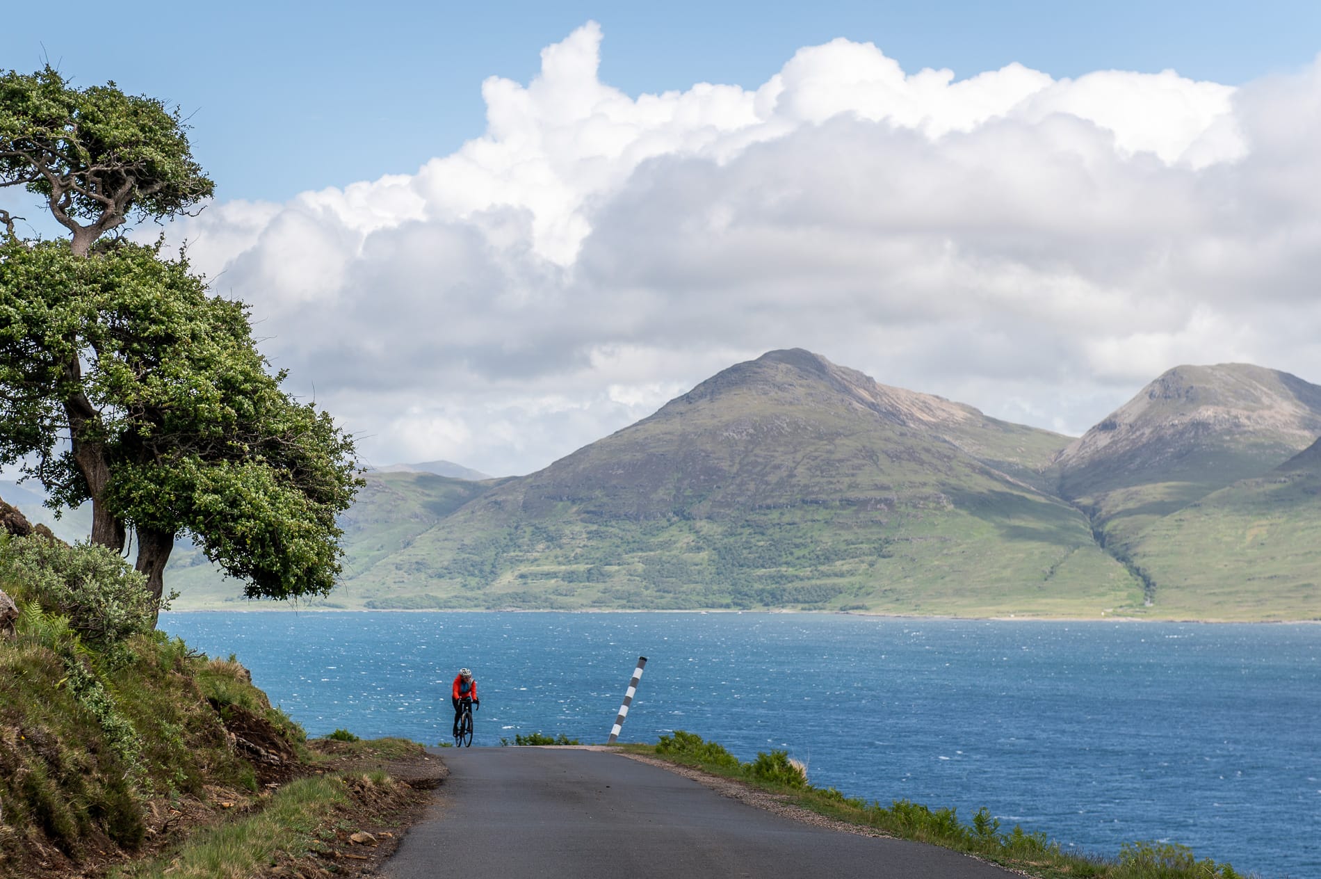 A cyclist riding around a loch with mountains in the background.